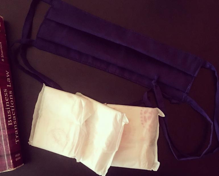 Three Sanitary Pads, cloth face masks and Law textbook on a black surface.