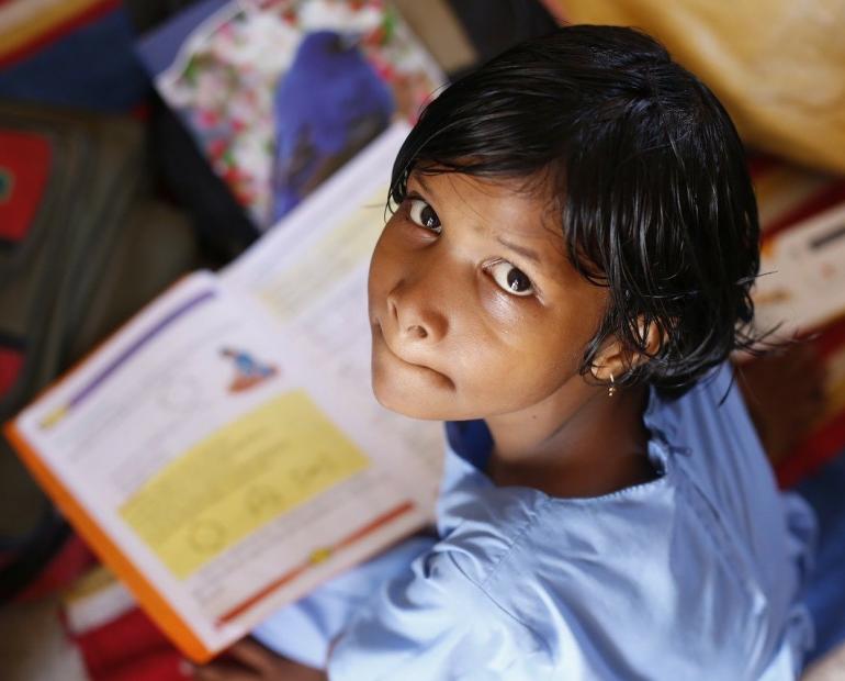 Young Indian girl with school book in front of her looking up.