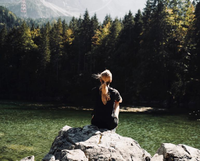 a woman in black shirt sitting on rock near green trees