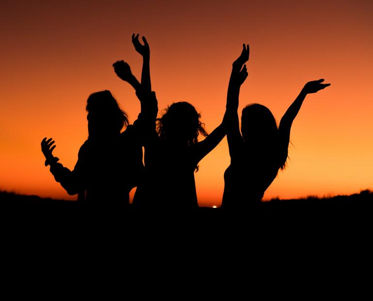 sihouette of three women with hands in air dancing