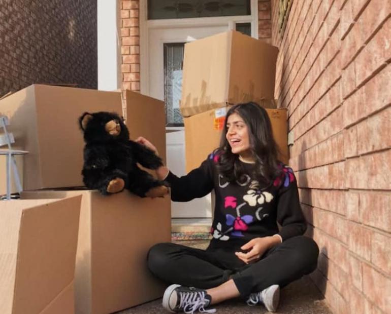 A photo of Aiza sitting next to a stack of boxes filled with teddy bears for children in need.