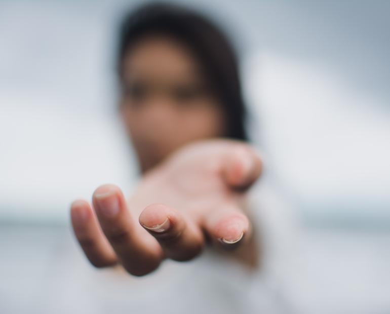 A person reaches out a hand towards the camera. The person is blurred and only the fingers of the hand are in focus