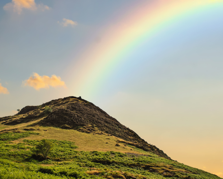 Green mountain with a rainbow in the blue sky